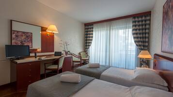 Une chambre d’hôtel avec deux lits, un bureau, une chaise, une télévision et une grande fenêtre avec des rideaux.