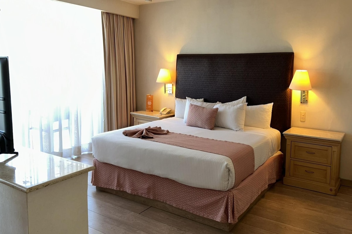 Une chambre d’hôtel avec un grand lit, des lampes de chevet, un bureau et une vue sur la ville.