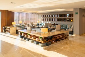 A modern lobby with a central seating area, bookshelves, and a reception desk.
