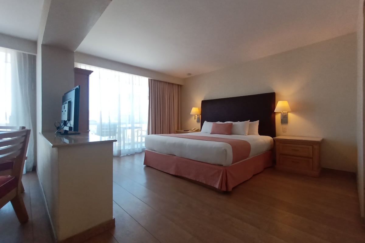 A hotel room with a bed, bedside tables, a desk, and a chair.