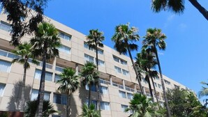 A multi-story hotel with a beige facade, numerous windows, and palm trees in the foreground.