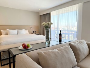 A hotel room with a large bed, a sofa, a table with a bottle and glasses, and a vase with flowers. - Wyndham Garden Tijuana Palacio Azteca (Tijuana)