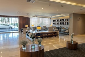Un hall d’hôtel moderne avec un comptoir d’accueil, un espace salon et une vue sur une voiture garée à l’extérieur.
