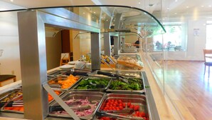 Zona de buffet con diversas opciones de comida, como ensaladas, frutas y verduras, en un ambiente moderno con separador de vidrio.