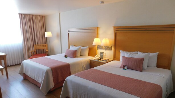A hotel room with two beds, each with a red and white bedspread, a wooden nightstand with a lamp, and a wooden chair.
