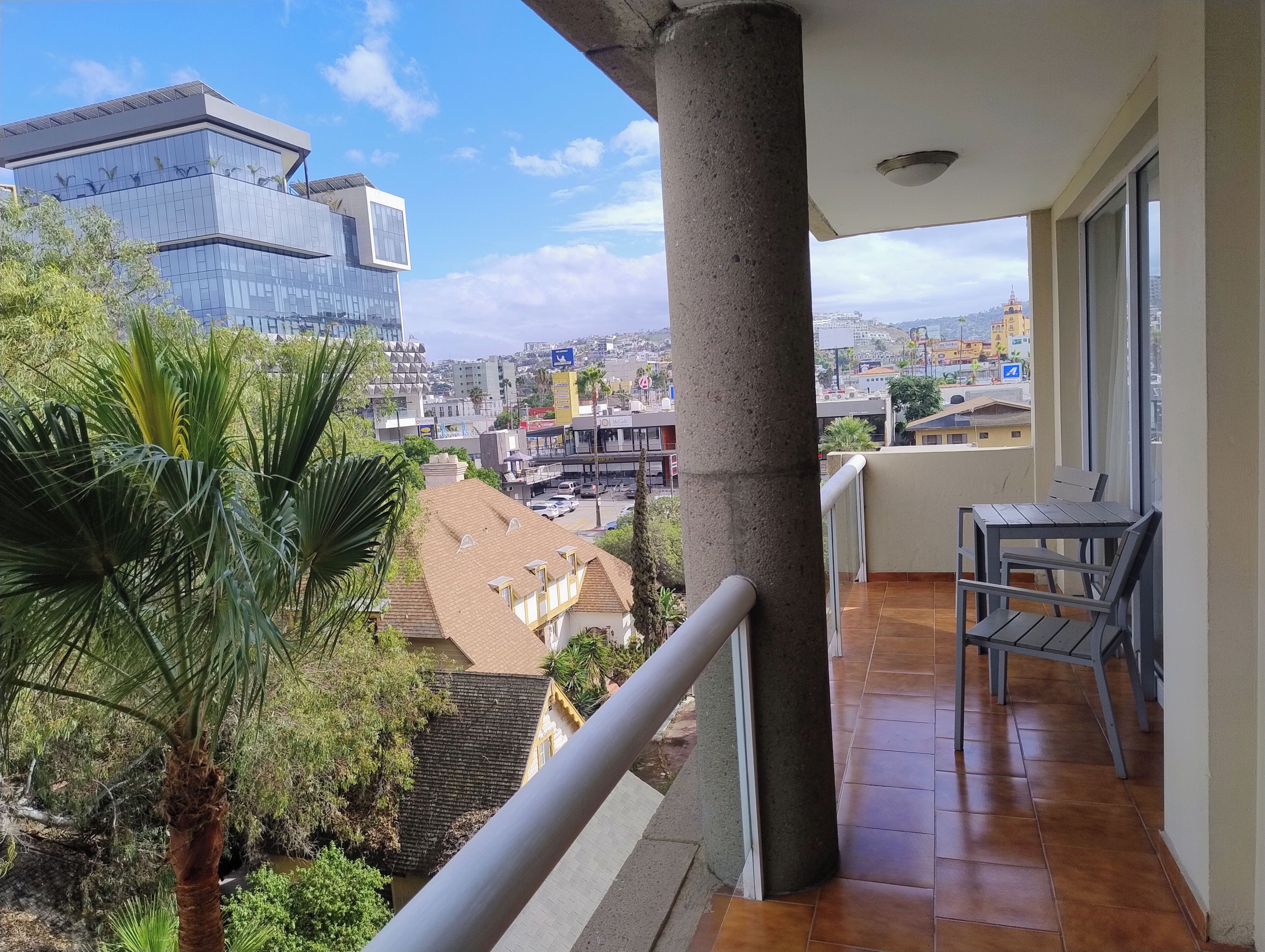 A balcony with a view of a cityscape, including modern buildings and a palm tree.