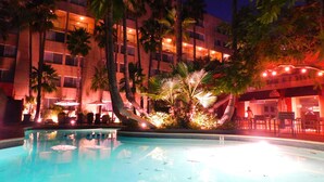 A swimming pool surrounded by palm trees and a building with multiple balconies.