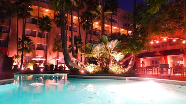 Una piscina rodeada de palmeras y un edificio con varios balcones.