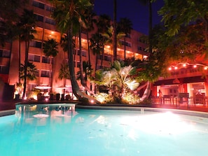 A swimming pool surrounded by palm trees and a building with multiple balconies.