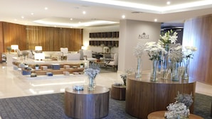 Un moderno vestíbulo de hotel con una zona de estar central, varias mesas redondas de madera con jarrones y un mostrador de recepción.