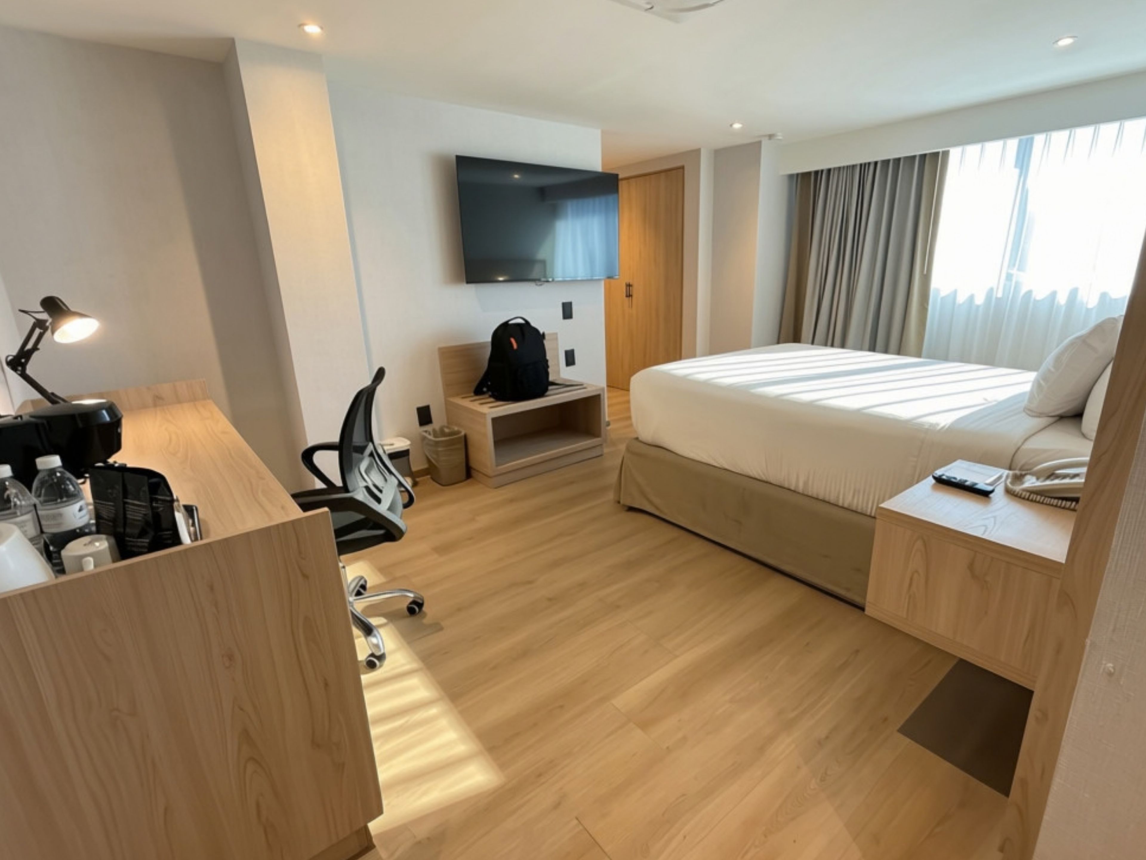 Habitación de hotel con cama, escritorio, silla, televisor y ventana con cortinas.