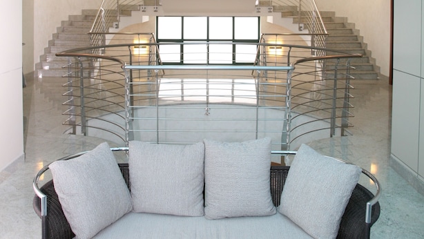 A modern interior with a curved staircase, a sofa with cushions, and a glass railing. - Hotel Parisi (Nichelino)