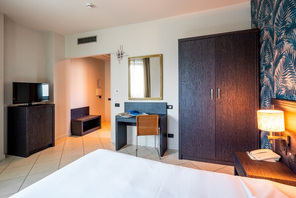 A hotel room with a bed, a desk with a chair, a wardrobe, a television, and a lamp.