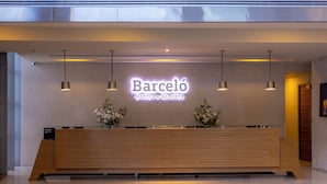 A modern reception desk with a 'Barceló Hotels & Resorts' sign, two potted plants, and pendant lighting. - Barceló México Santa Fe (Mexico City)