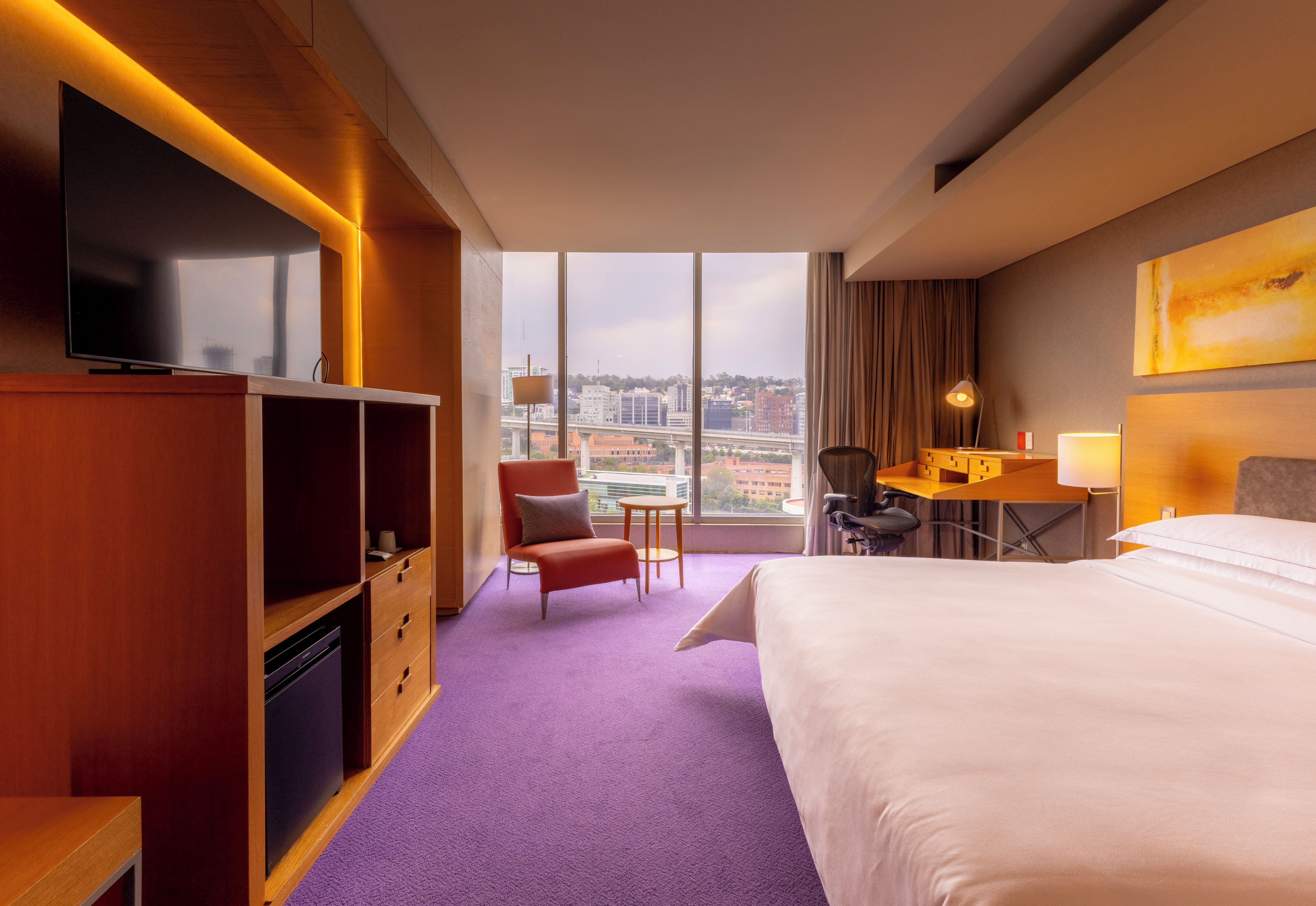 Una habitación de hotel con cama, escritorio, silla, televisión y vistas de la ciudad.