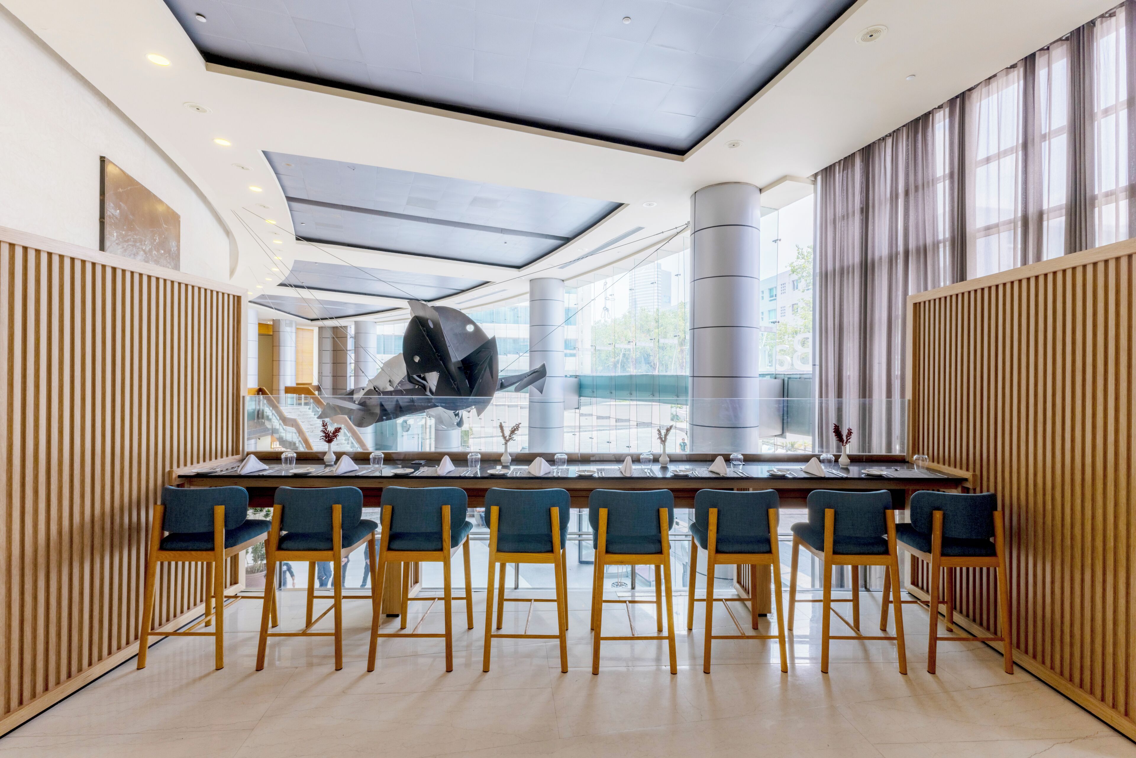 A modern dining area with a long table, multiple chairs, and a view of the city through large windows.