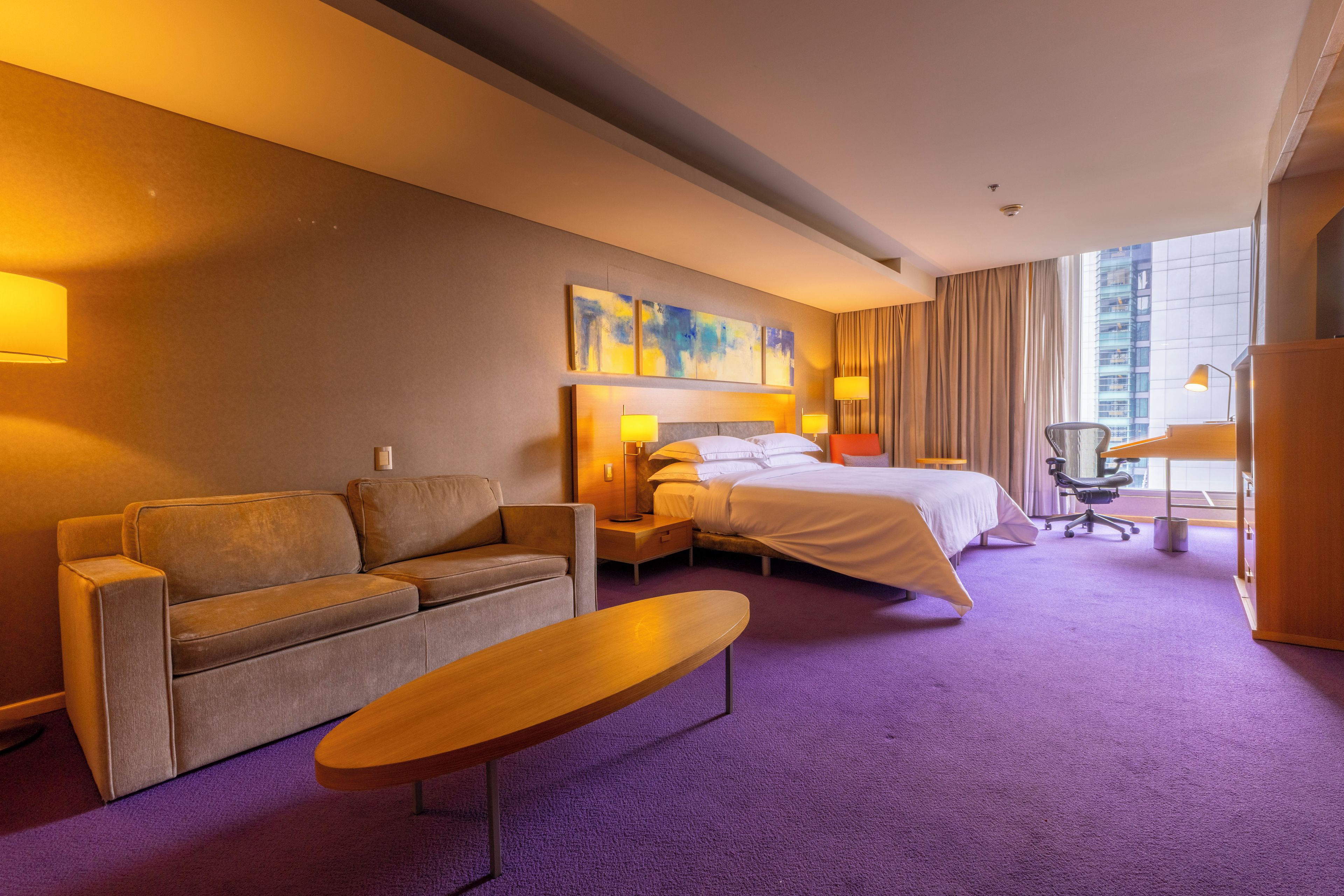 Una habitación de hotel con cama, sofá, una mesita y un escritorio con silla.