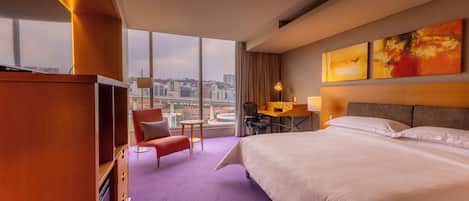 A hotel room with a large bed, a desk, a chair, and a view of the cityscape.