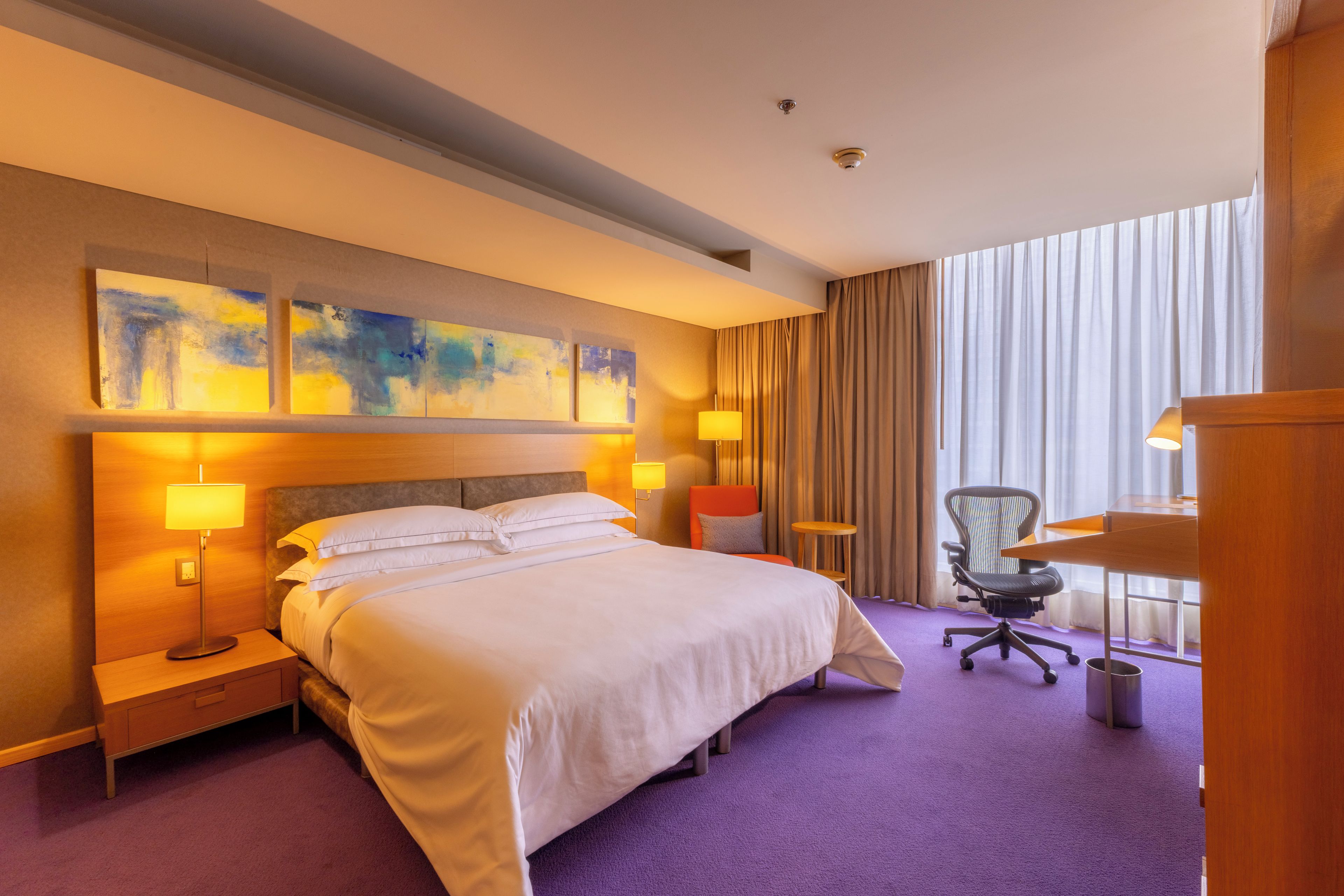 Habitación de hotel con una cama grande, dos lámparas de noche, un escritorio, una silla y una ventana con cortinas.