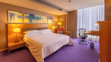 Habitación de hotel con una cama grande, dos lámparas de noche, un escritorio, una silla y una ventana con cortinas.