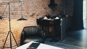 Egy modern nappali, melyben téglából készült fal, fekete bőrkanapé, fehér dohányasztal és fekete állólámpa található.