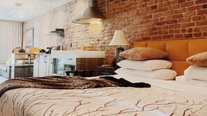 Egy modern hálószoba, melyben téglából készült fal található, egy nagy ágy, melyen faágak mintázatú ágytakaró van, egy íróasztal lámpával, és egy függesztett lámpatest.