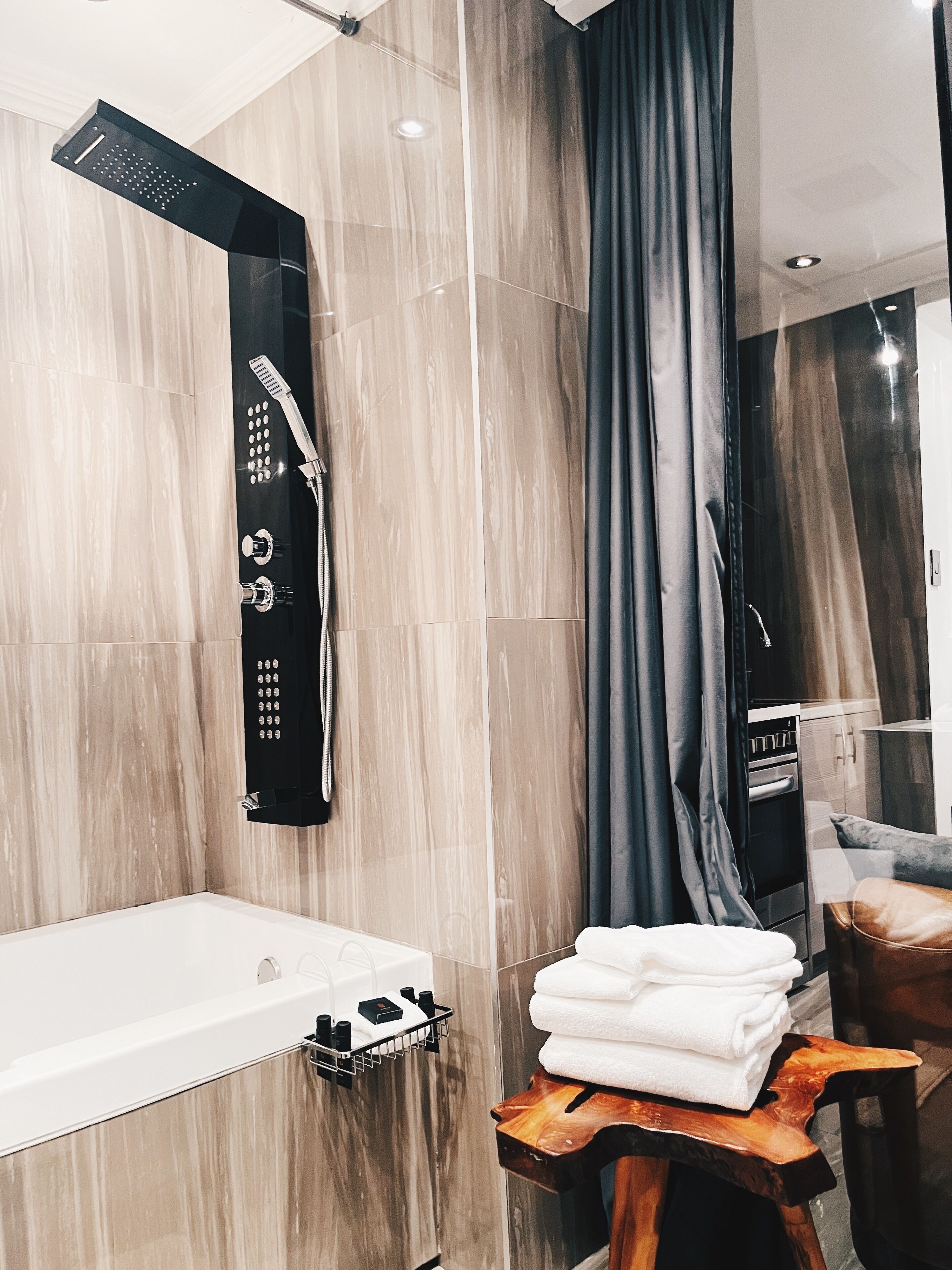 A modern bathroom with a bathtub, a shower with a rain showerhead, and a wooden stool with towels.