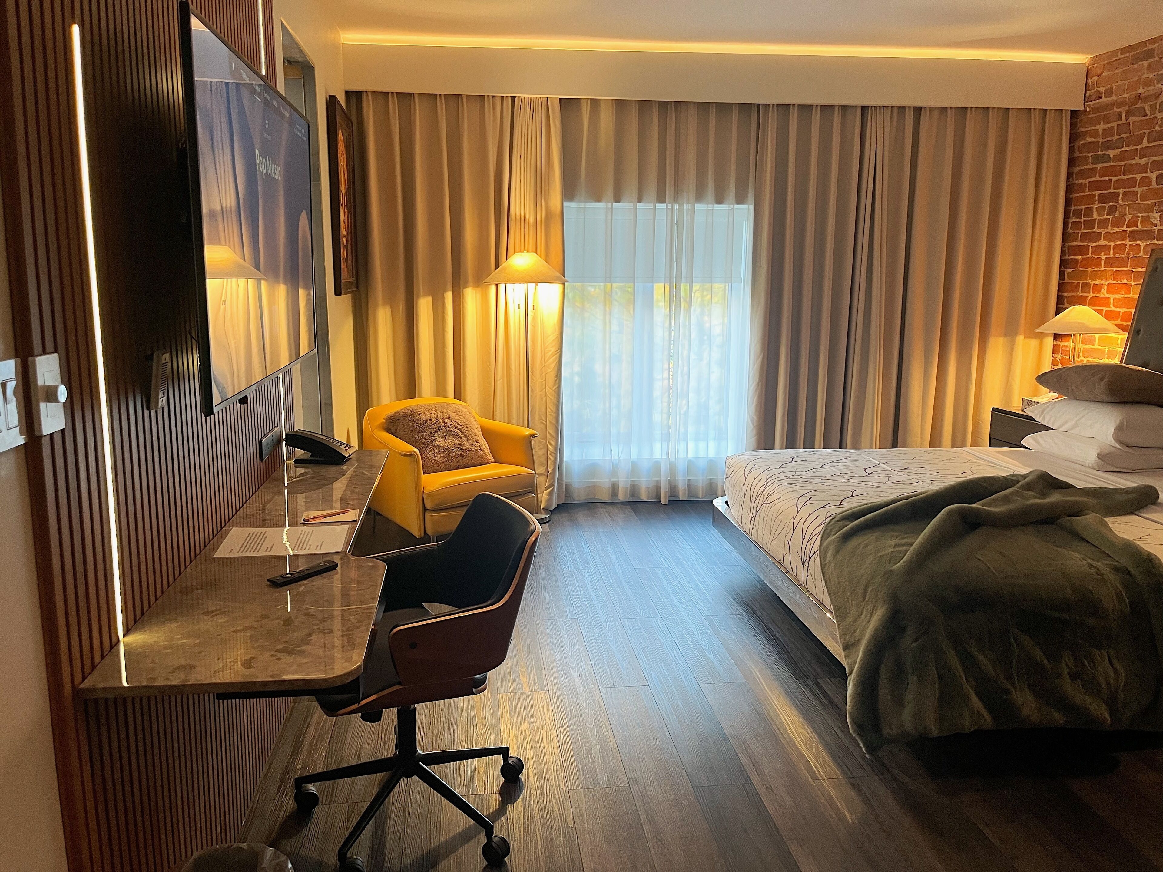 A hotel room with a bed, a desk with a chair, a television, and a window with curtains.