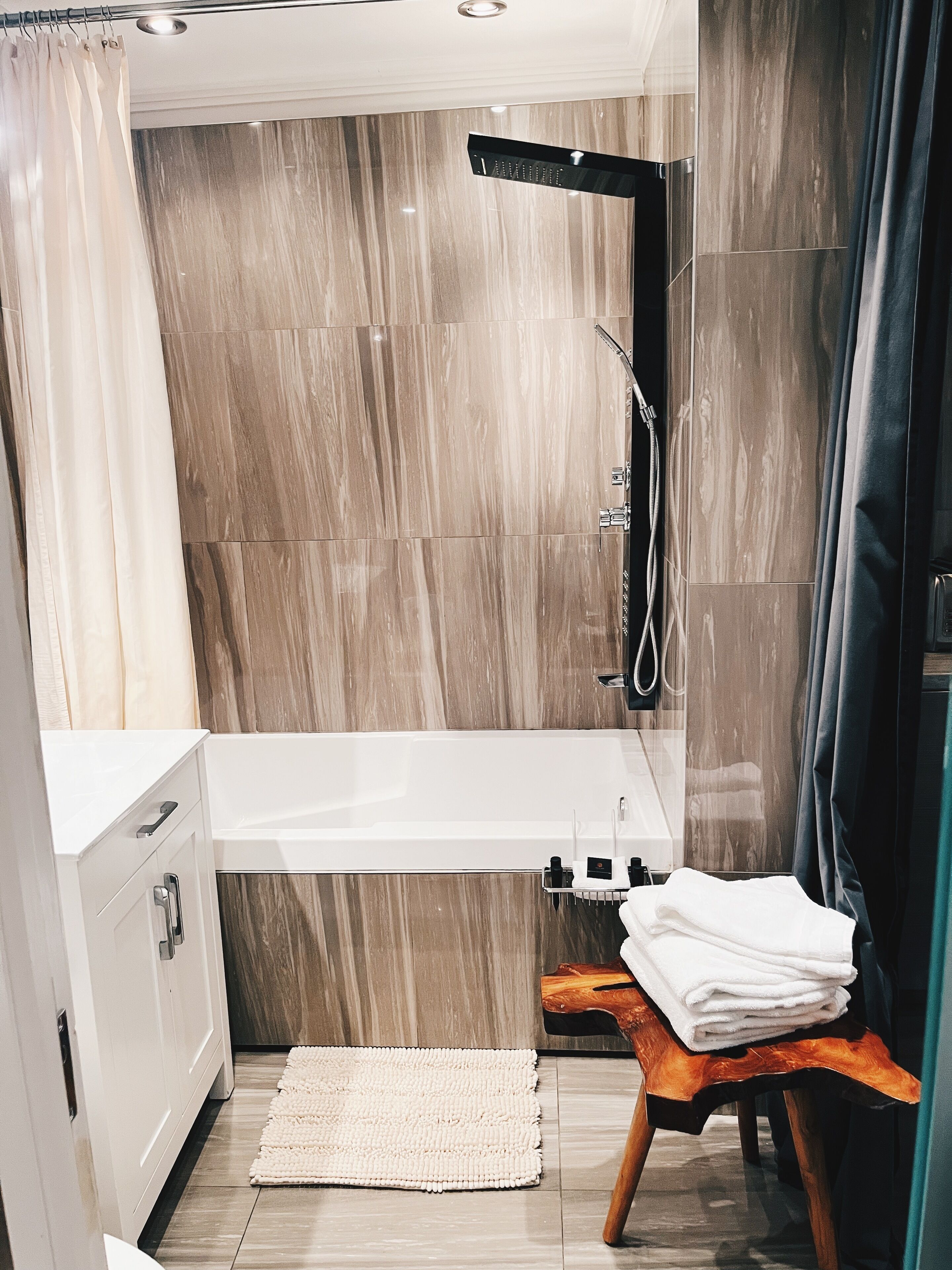 Un baño moderno con bañera, ducha y un taburete de madera con toallas.