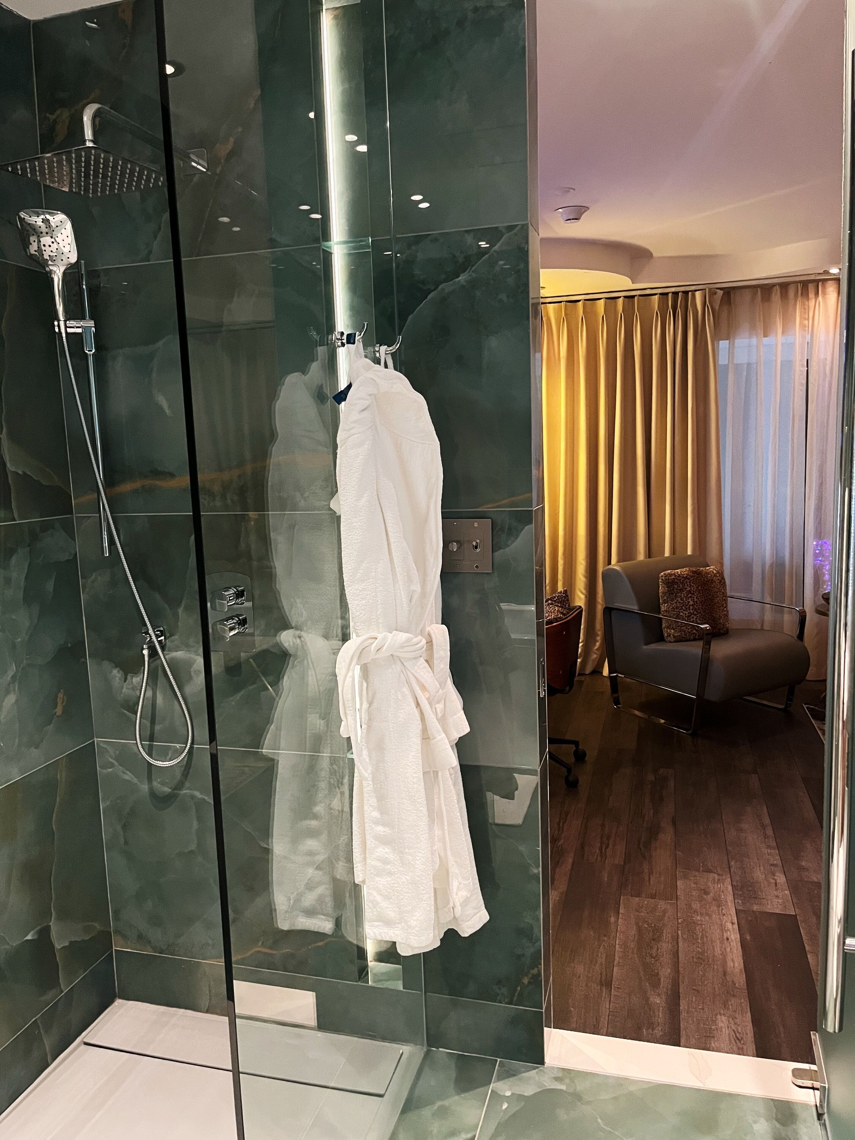 A glass-enclosed shower with a handheld showerhead and a towel rack with a white towel.