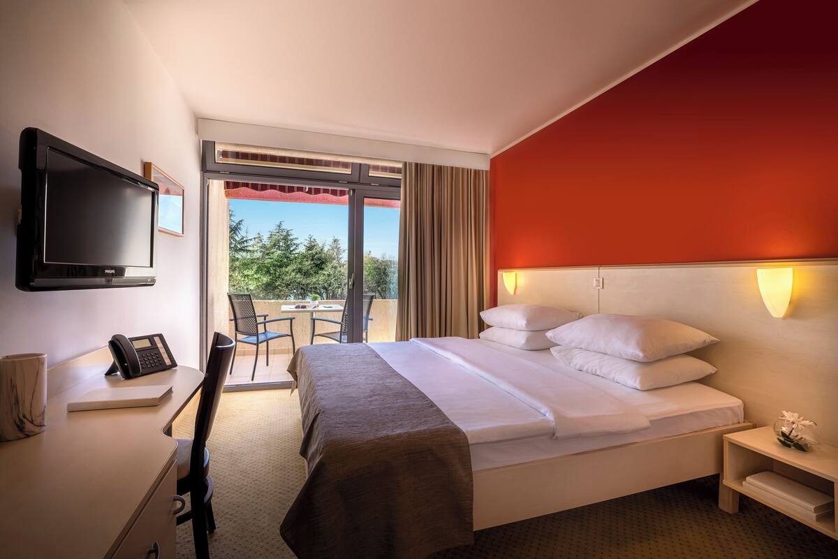 A hotel room with a bed, bedside table, TV, and a desk with a phone.