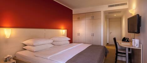 Una habitación de hotel con una cama grande, un escritorio con una silla, un televisor y un armario.