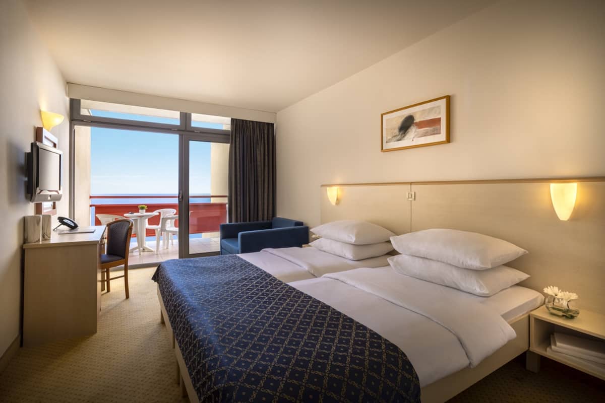 A hotel room with a large bed, a desk, a chair, and a view of the outside.