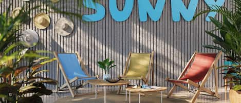 A sunlit room with a striped wall, three beach chairs, a small table, and a large potted plant.