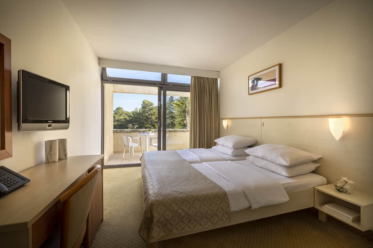 A hotel room with a bed, desk, chair, and a TV.