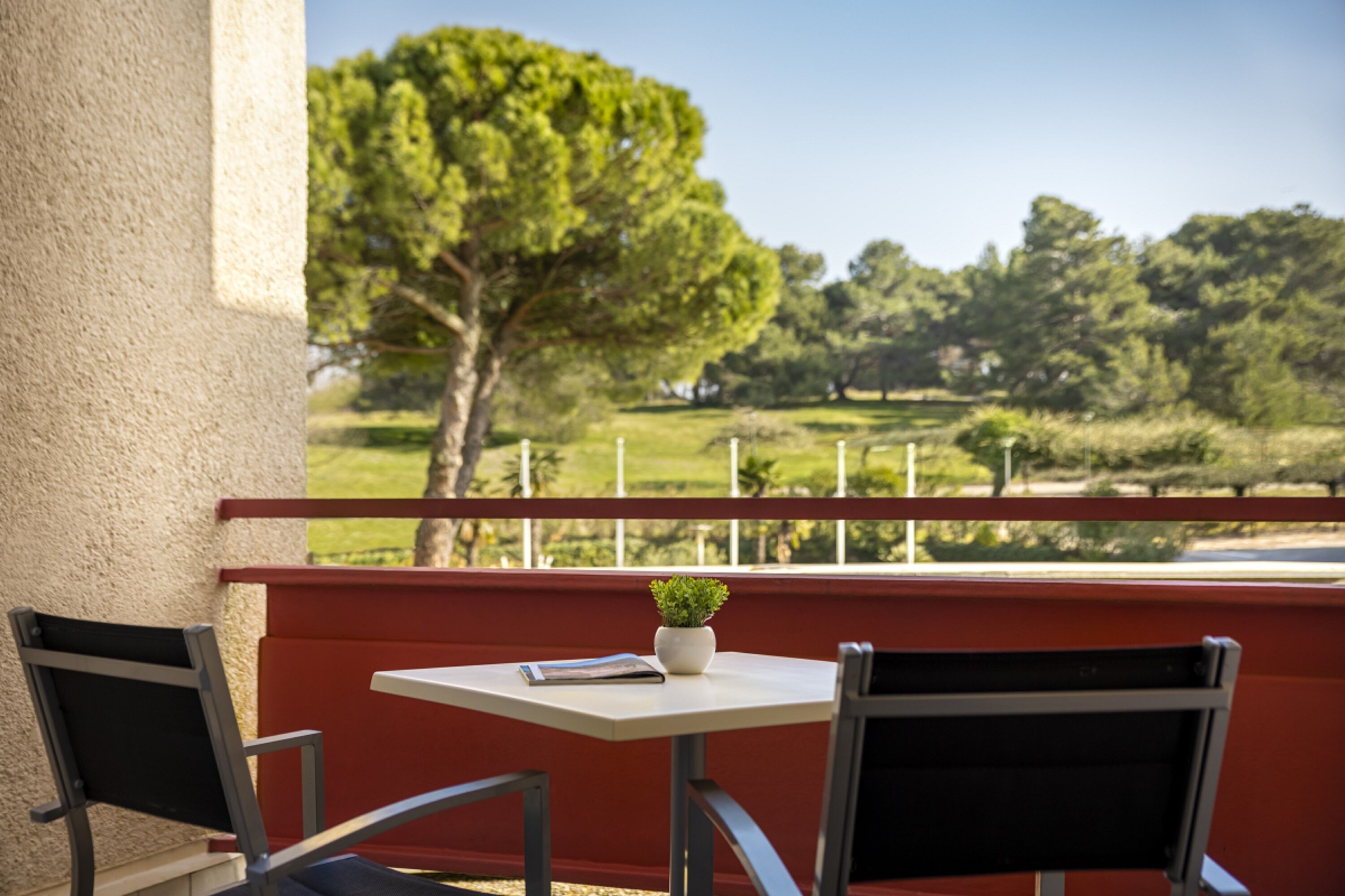A balcony with a table and two chairs, a potted plant, and a view of a green landscape.