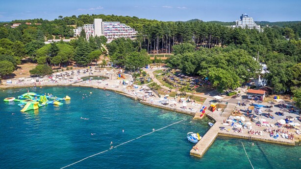 An aerial view of a coastal resort with a beach, swimming area, and a pier. - Rubin Sunny Hotel (Porec)