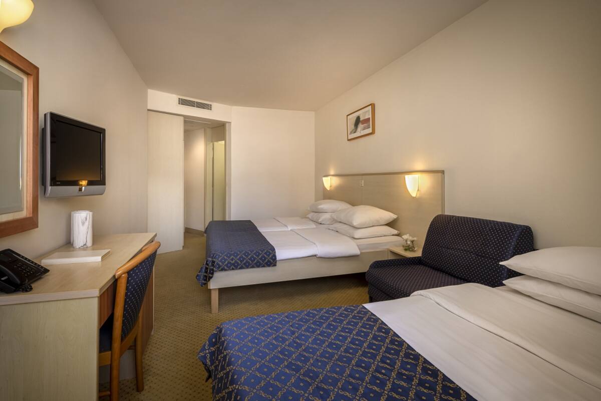 A hotel room with a desk, two beds, a TV, and a framed picture on the wall.