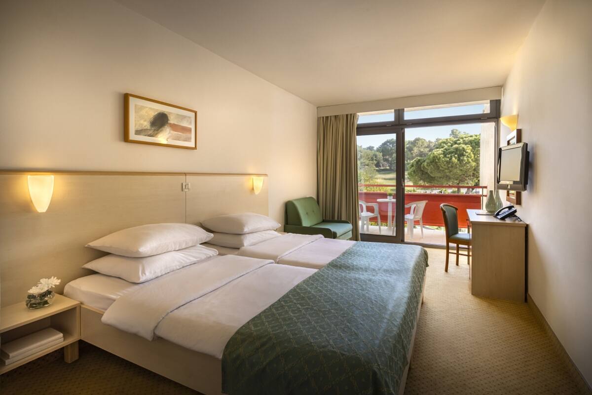 A hotel room with two beds, a desk, a chair, and a balcony with a table and chairs.