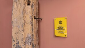 Un letrero amarillo con texto sobre una pared rosa, sujeto a una puerta de madera con un pestillo metálico.