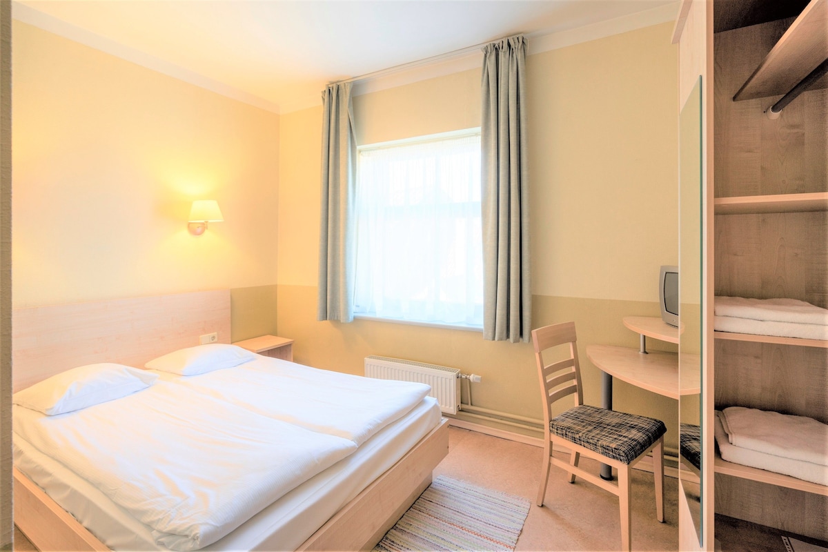 A hotel room with a bed, a chair, a desk, and a wardrobe.