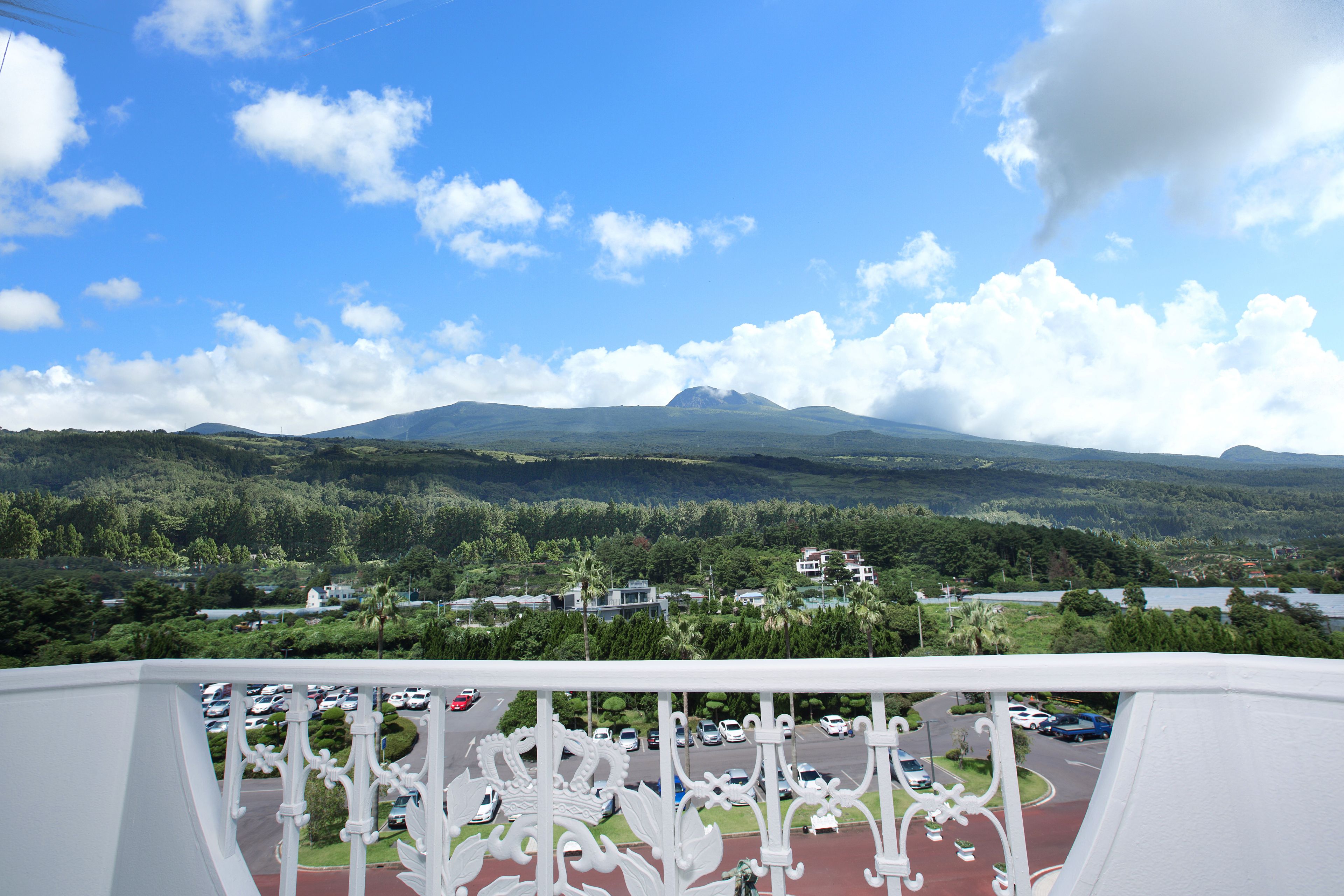 A balcony with a view of a parking lot, a mountain, and a lake.