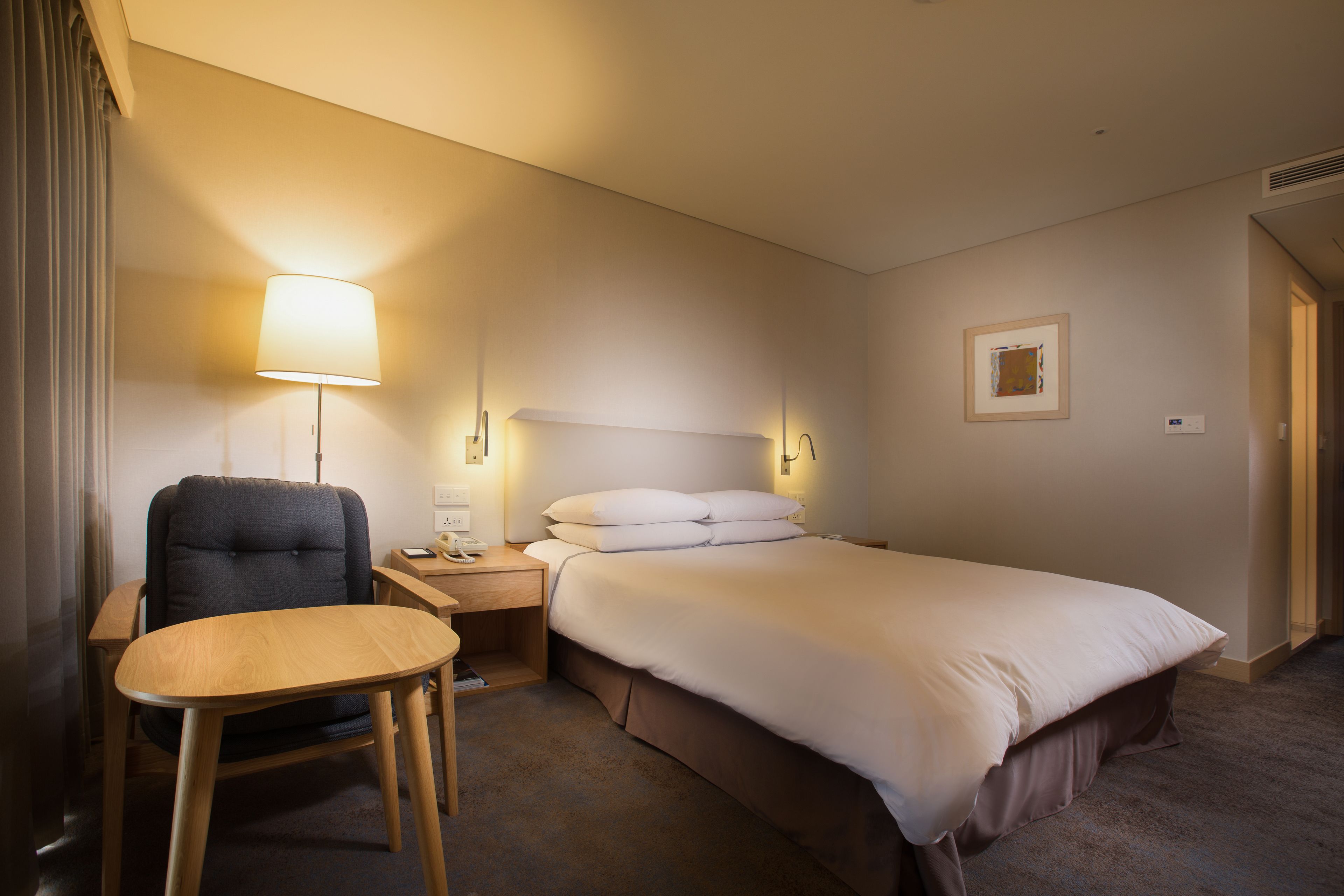 Una habitación de hotel con una cama, un escritorio con silla, una lámpara y una mesita de noche.