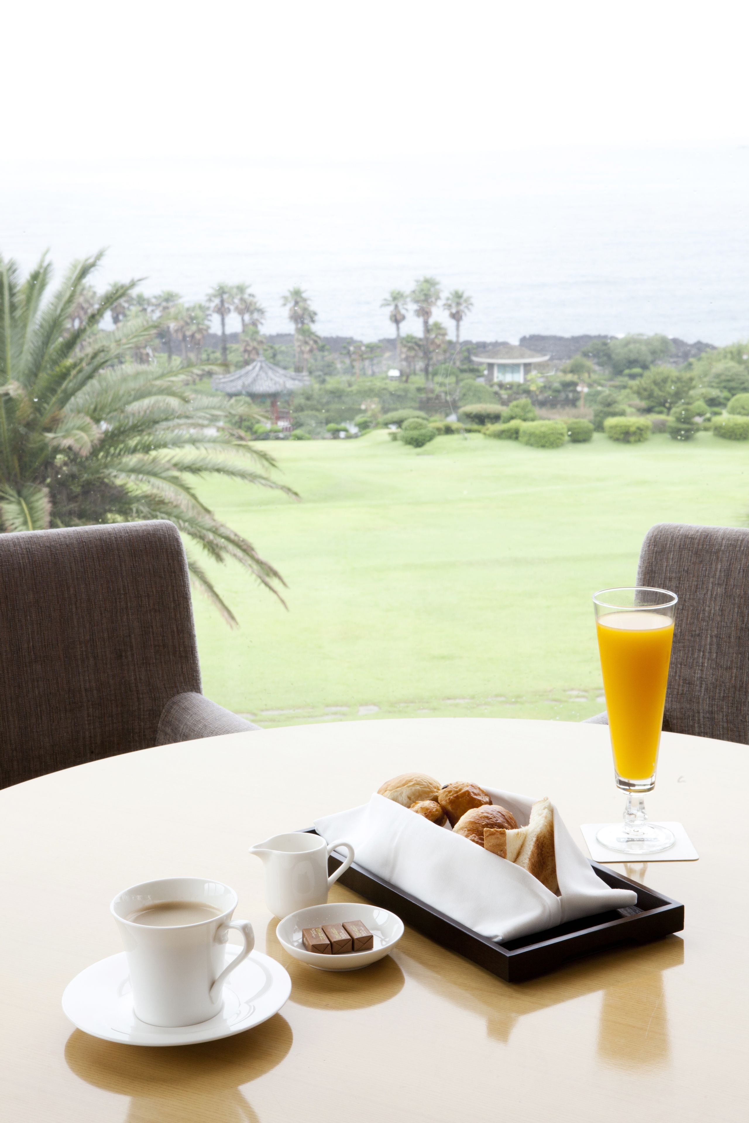 A table with breakfast items, a glass of orange juice, and a view of a golf course and ocean.