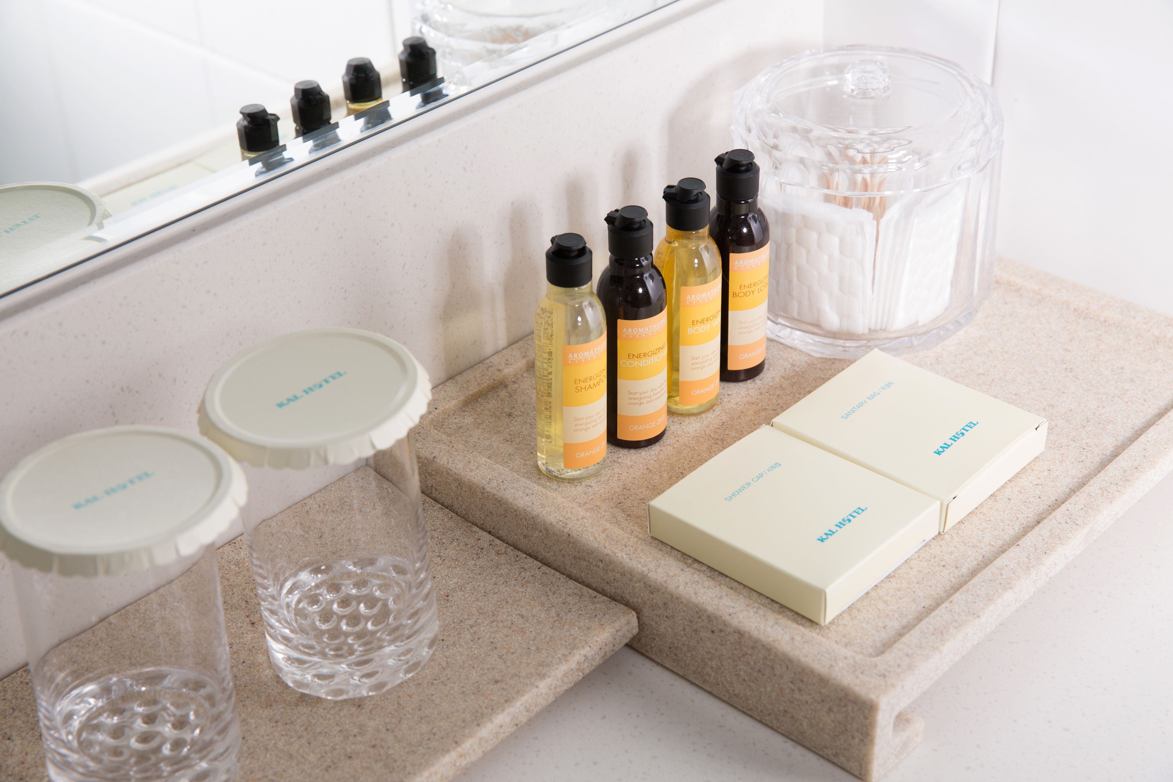 Una encimera de baño con artículos de aseo, incluyendo botellas y cajas, además de un recipiente de vidrio.