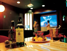 Un bar con botellas de whisky, un plato de fruta y una pantalla de televisión al fondo.