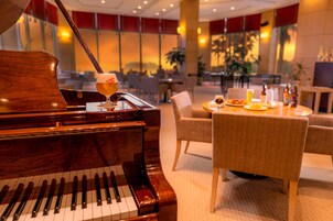 Un piano de cola con una jarra de cerveza encima, una mesa de comedor con comida y bebidas, y una zona de estar acogedora en un vestíbulo bien iluminado.