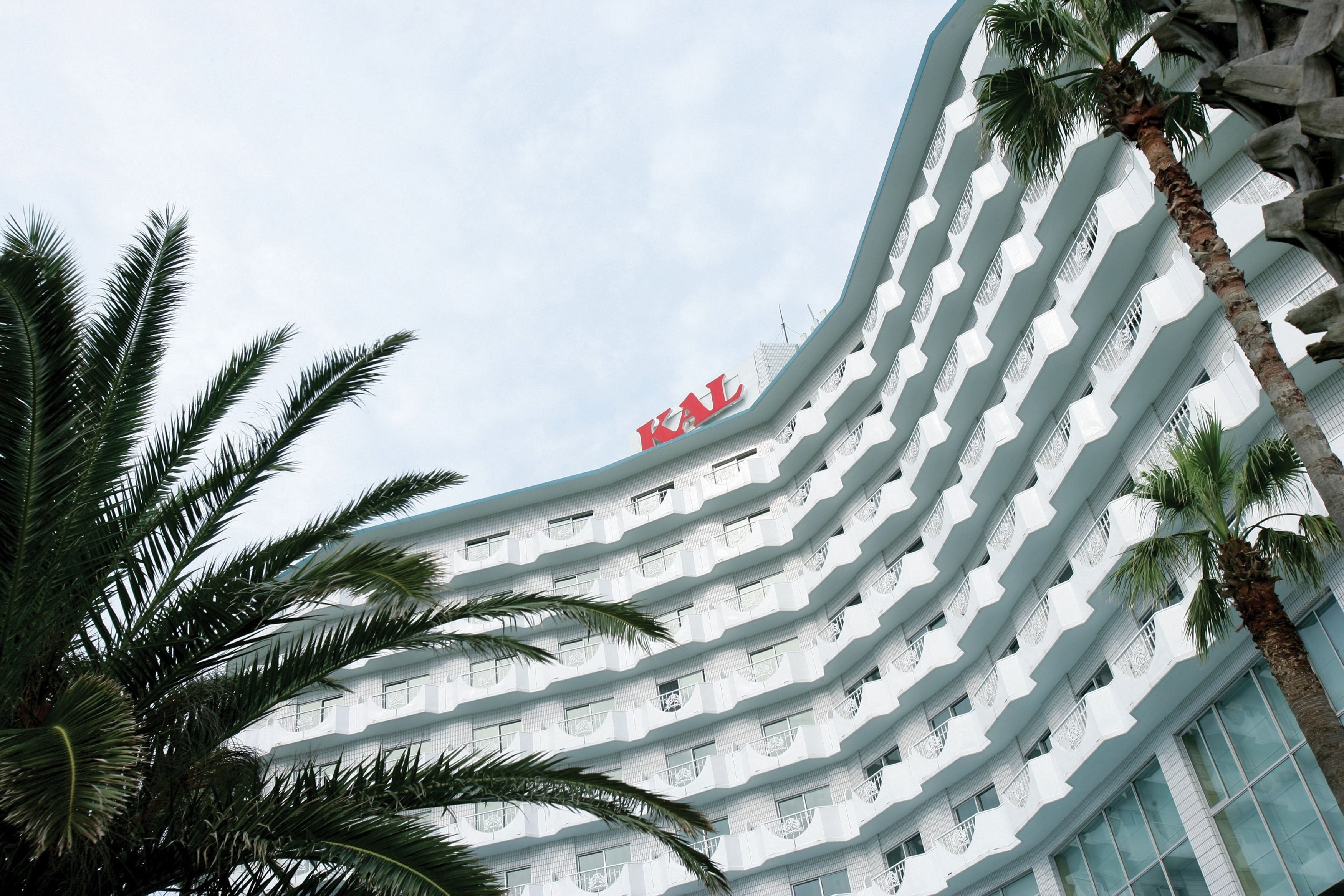 A multi-story hotel with a curved facade, balconies, and palm trees.