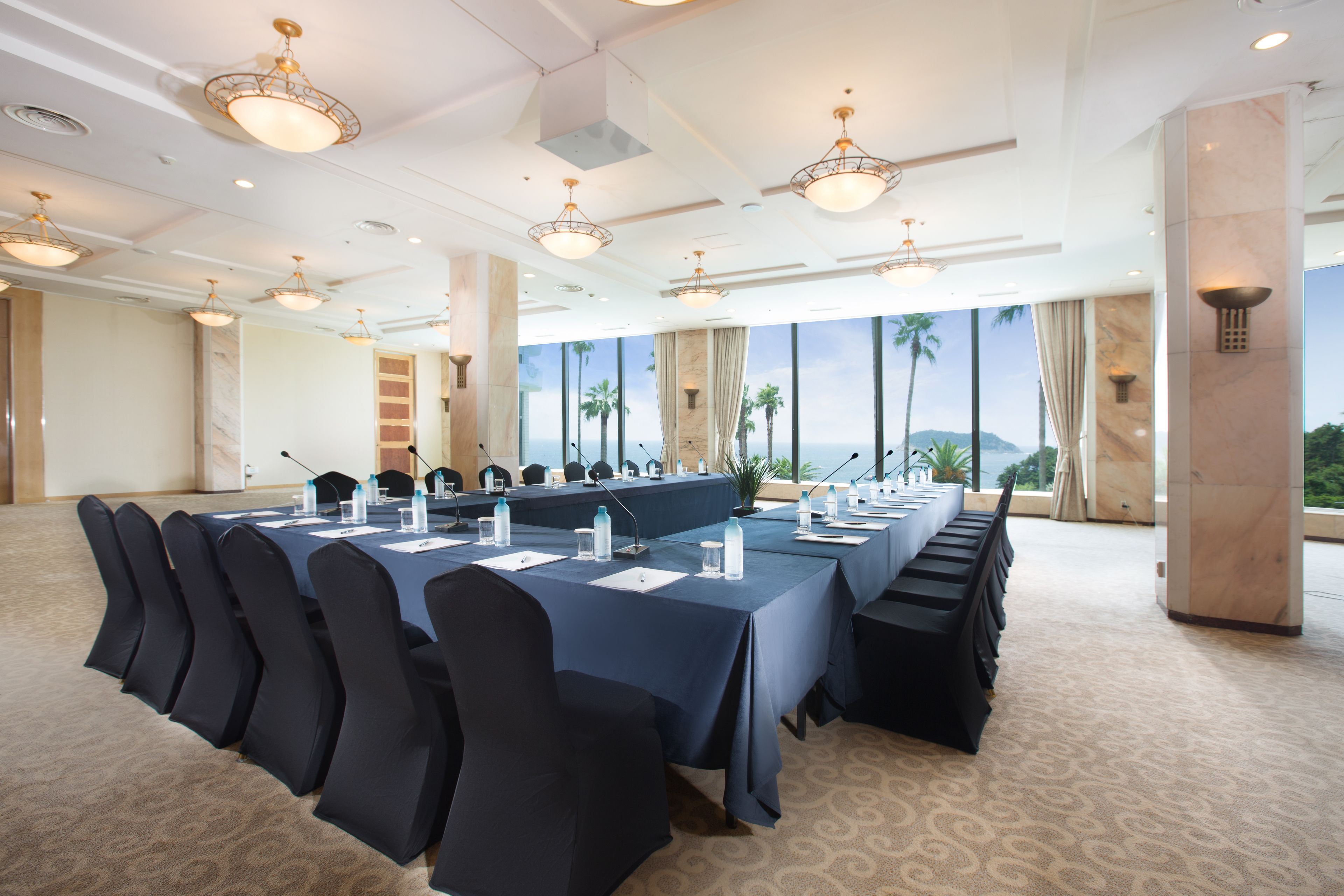 A conference room with a long table, black chairs, microphones, and water bottles.