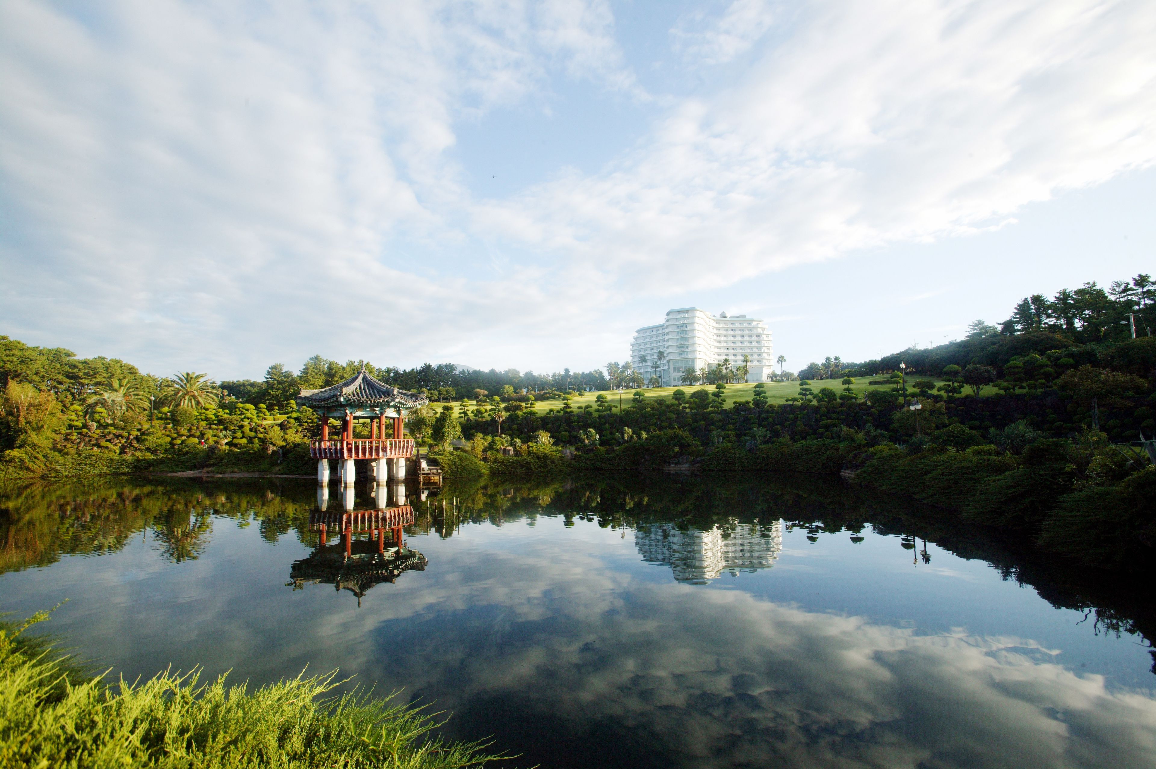 A serene lake with a traditional pavilion and a modern building in the background.